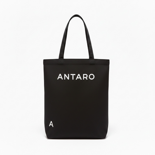 A black canvas tote bag with two top handles, featuring the brand name 'ANTARO' printed in white capital letters on the front, and a small white letter 'A' near the bottom left. The bag is photographed against a clean, solid white background.